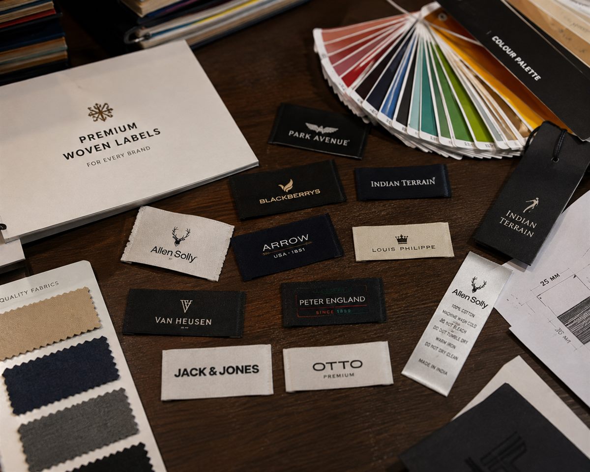 Premium woven label samples for leading apparel brands laid out beside a Pantone colour palette and fabric swatches — Shree Krishna Labels sampling